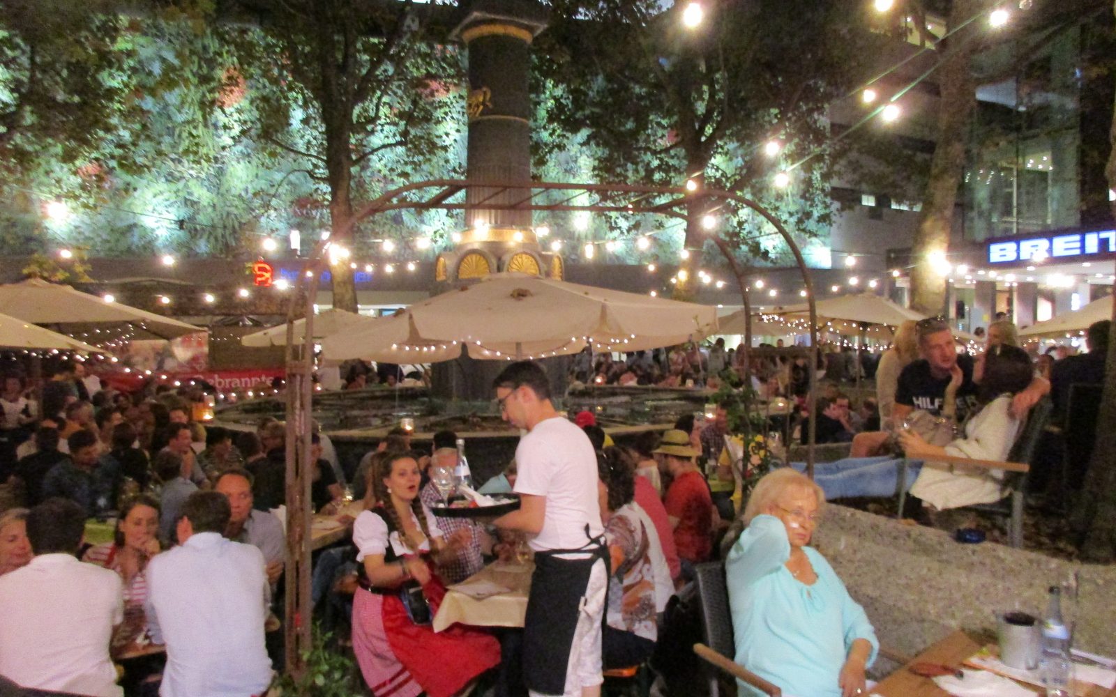 Stuttgarter Weindorf am Abend - besetzte Tische unter Sonnenschirmen und Lichterketten